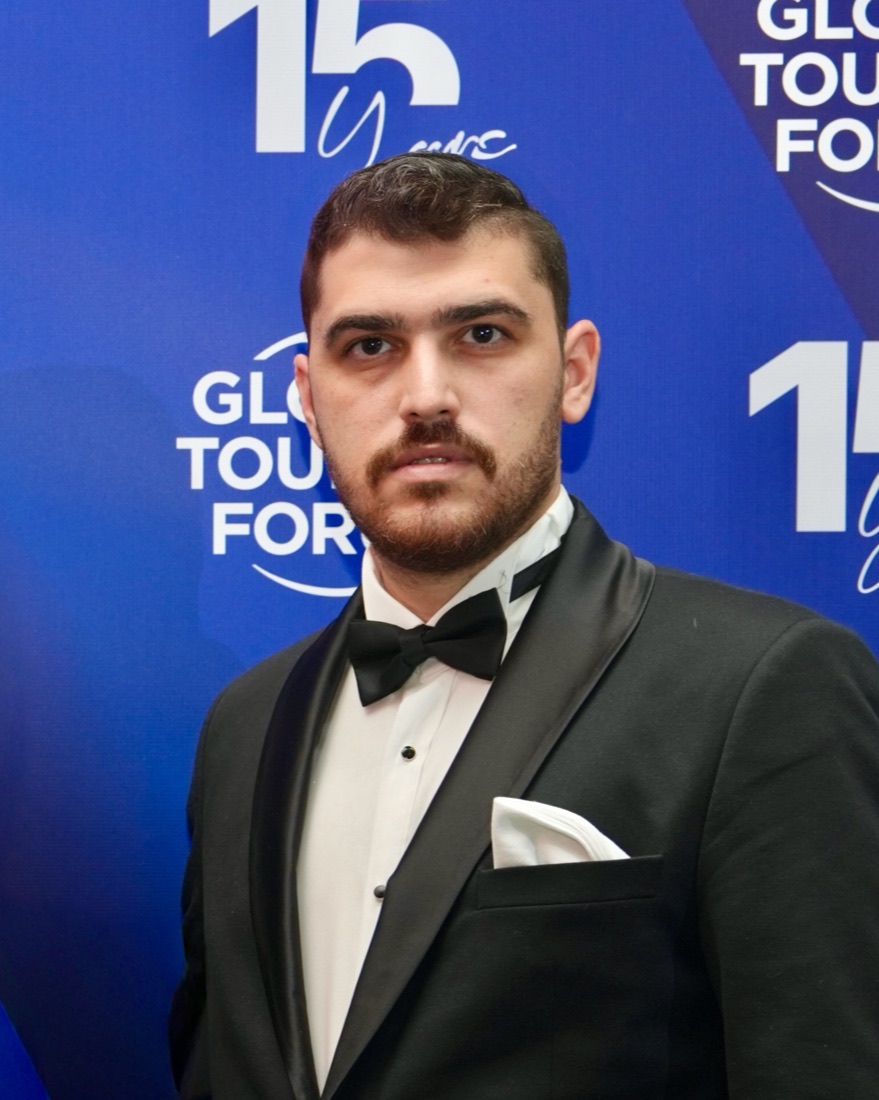 Musa Toktaş in a black tuxedo and bow tie in front of a blue Global Tourism Forum backdrop