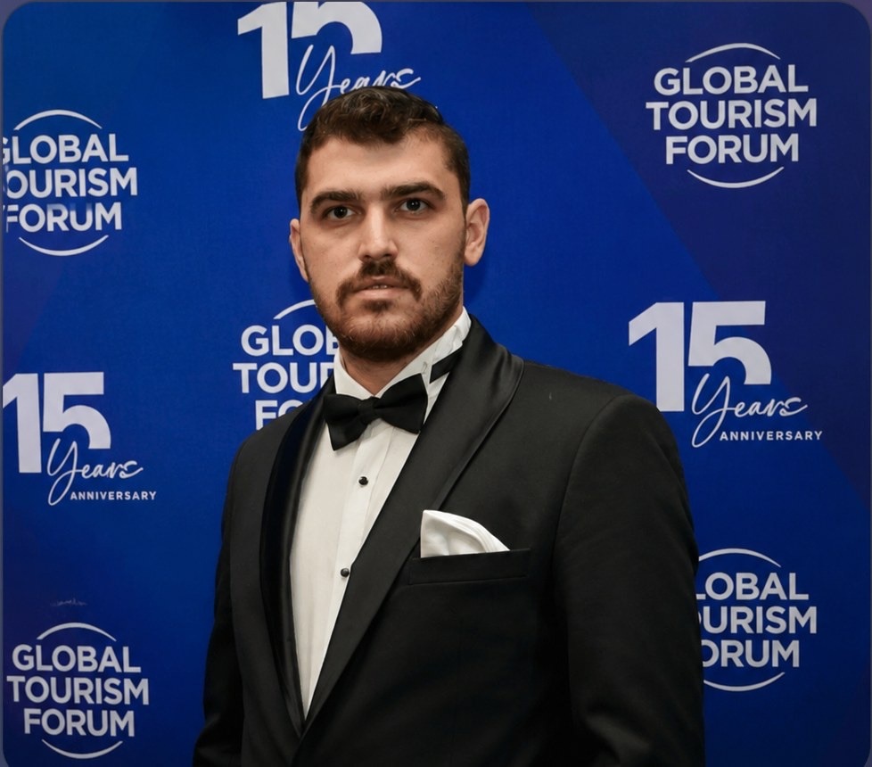 Musa Toktaş in a black tuxedo in front of a Global Tourism Forum backdrop