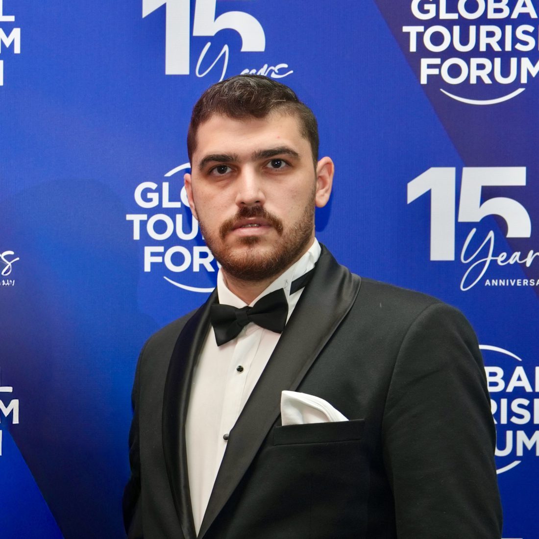 Musa Toktaş in a black tuxedo and bow tie in front of a blue Global Tourism Forum backdrop